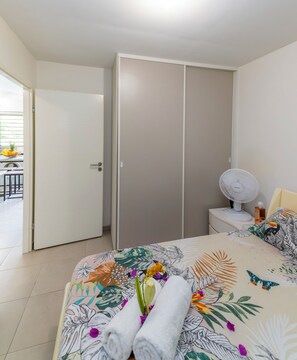 A bedroom with a bed, a bedside table with a lamp, a fan, and a wardrobe. - Pom'kanelle (Le Gosier)