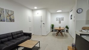 Moderni olohuone, jossa on musta sohva, puinen sohvapöytä ja ruokailutila, jossa on pyöreä pöytä ja tuolit.