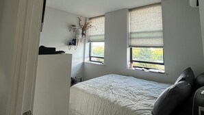 Ein Schlafzimmer mit einem Bett, einem Schreibtisch und zwei Fenstern mit Jalousien.