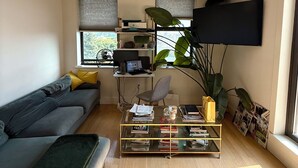 Ein modernes Wohnzimmer mit einer Couch, einem Couchtisch mit Büchern, einem Fernseher und einer großen Pflanze.