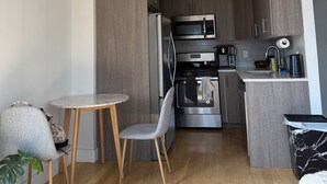 Eine moderne Küche mit dunklen Holdekor-Schränken, Edelstahlgeräten und einer kleinen Essecke mit rundem Tisch und zwei Stühlen.