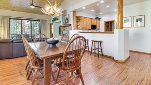 A spacious dining area with a wooden table and chairs, a built-in kitchen with wooden cabinets, and a large window offering a view of the outdoors. - Hot Tub, Deck & Grill! Mtn Retreat in Show Low (Show Low)