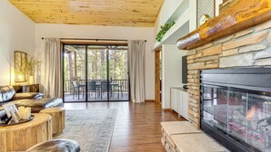 A spacious living room with a stone fireplace, leather sofas, and a large sliding glass door leading to an outdoor patio. - Hot Tub, Deck & Grill! Mtn Retreat in Show Low (Show Low)