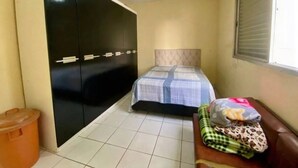 A small, compact room with a bed, a wardrobe, a ceiling fan, and a window. - Cozy and very well-located apartment in a condominium. (Praia Grande)