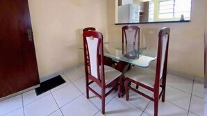 A dining area with a glass table and four wooden chairs. - Cozy and very well-located apartment in a condominium. (Praia Grande)
