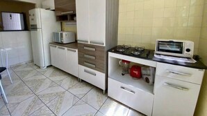 A compact kitchen with white cabinets, a microwave, a gas stove, and a refrigerator. - Cozy and very well-located apartment in a condominium. (Praia Grande)