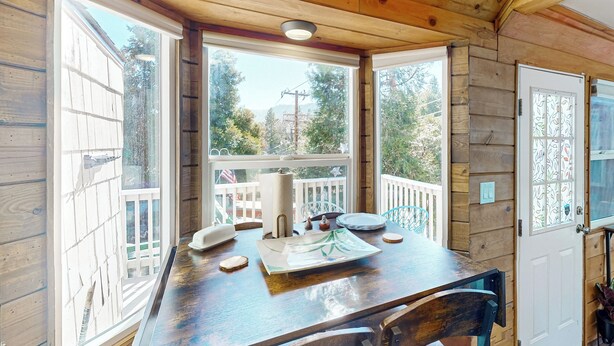 Una cabaña de madera con comedor que incluye una mesa, sillas y vistas del bosque circundante.