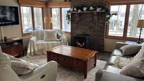 A cozy living room with a fireplace, leather sofas, a wooden coffee table, and a TV on the wall.