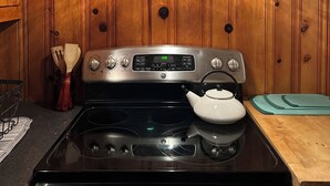 A kitchen with a stove, wooden panel walls, a hanging light, and a cutting board.
