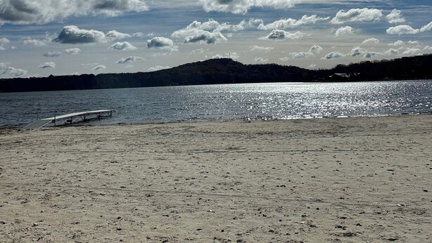 A beach with a clear sky, a sun shining, and a calm sea.