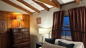 A bedroom with a bed, a dresser, a nightstand, a lamp, and a window with curtains.