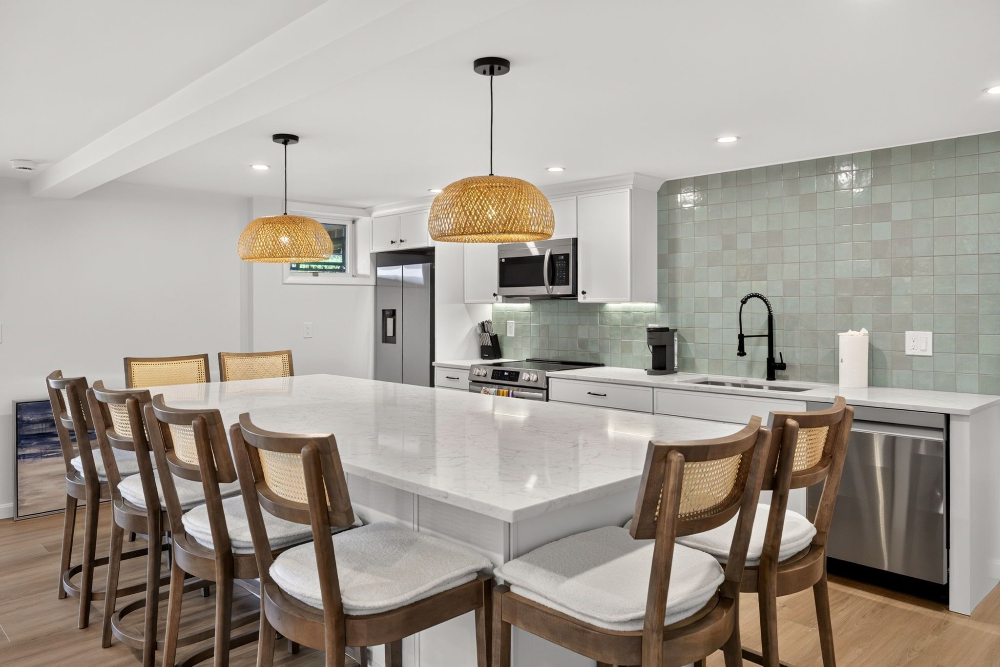 A modern kitchen with white cabinets, a large island, stainless steel appliances, and wicker pendant lights.