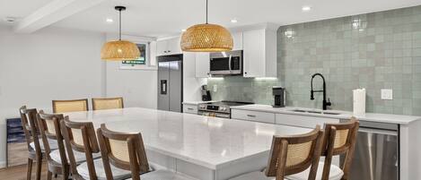 A modern kitchen with white cabinets, a large island, stainless steel appliances, and wicker pendant lights.
