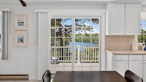 A kitchen with white cabinets, a dark wooden table, and a view of a lake through large windows. - 5 Bedrooms | Water Views | Private Pond Beach (Brewster)
