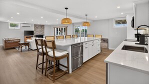 A spacious kitchen with a central island, wooden chairs, and pendant lighting. - 5 Bedrooms | Water Views | Private Pond Beach (Brewster)