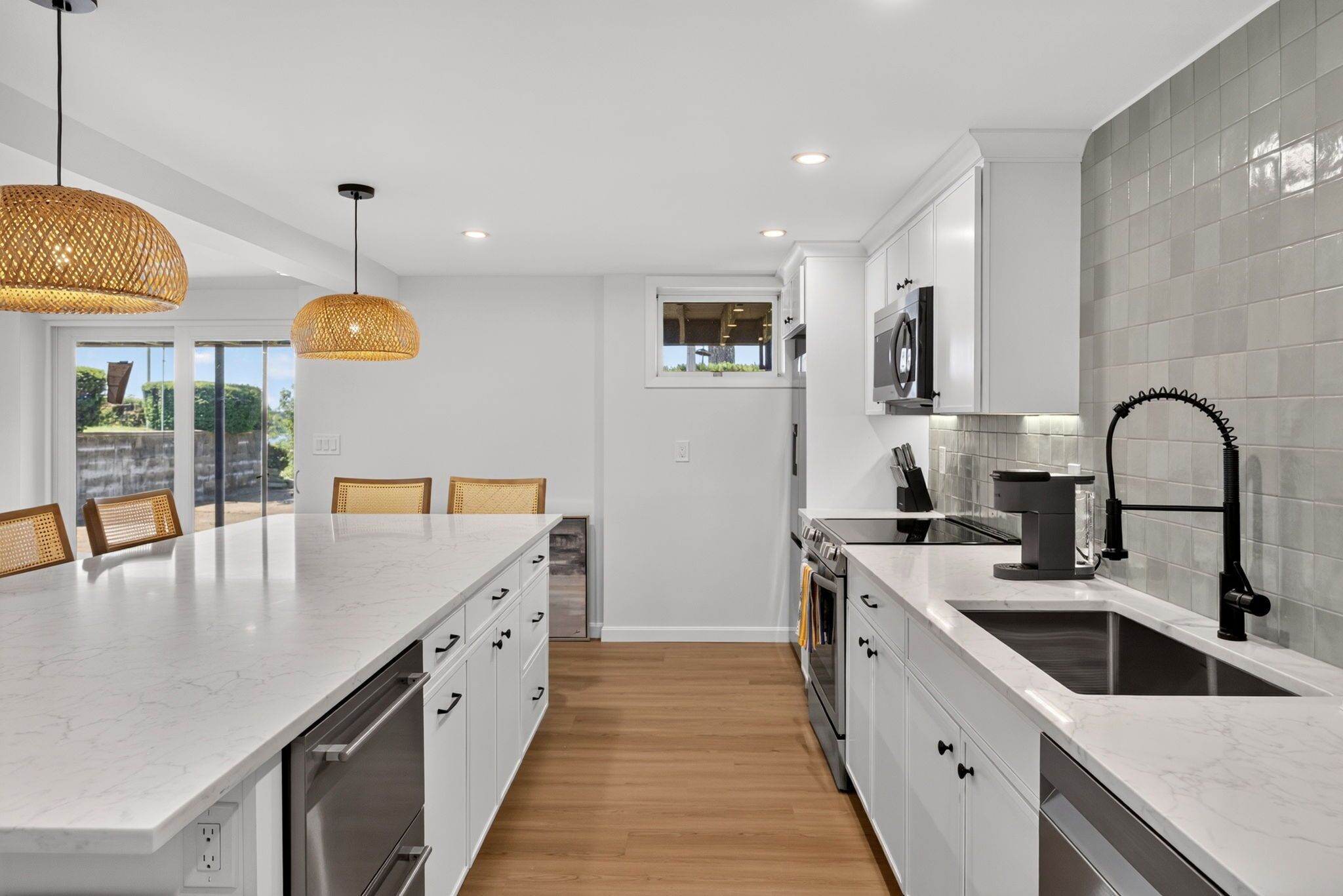 Une cuisine moderne avec des meubles blancs, un grand îlot central et une vue sur l’extérieur.