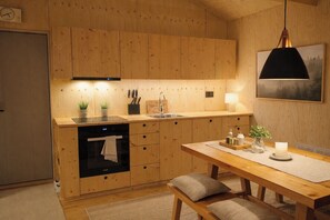 A modern kitchen with wooden cabinetry, a built-in oven, a sink, and a dining area with a table and bench.