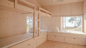 L’intérieur d’une cabane en bois, avec des lits superposés, une fenêtre donnant sur un paysage et un luminaire au plafond.