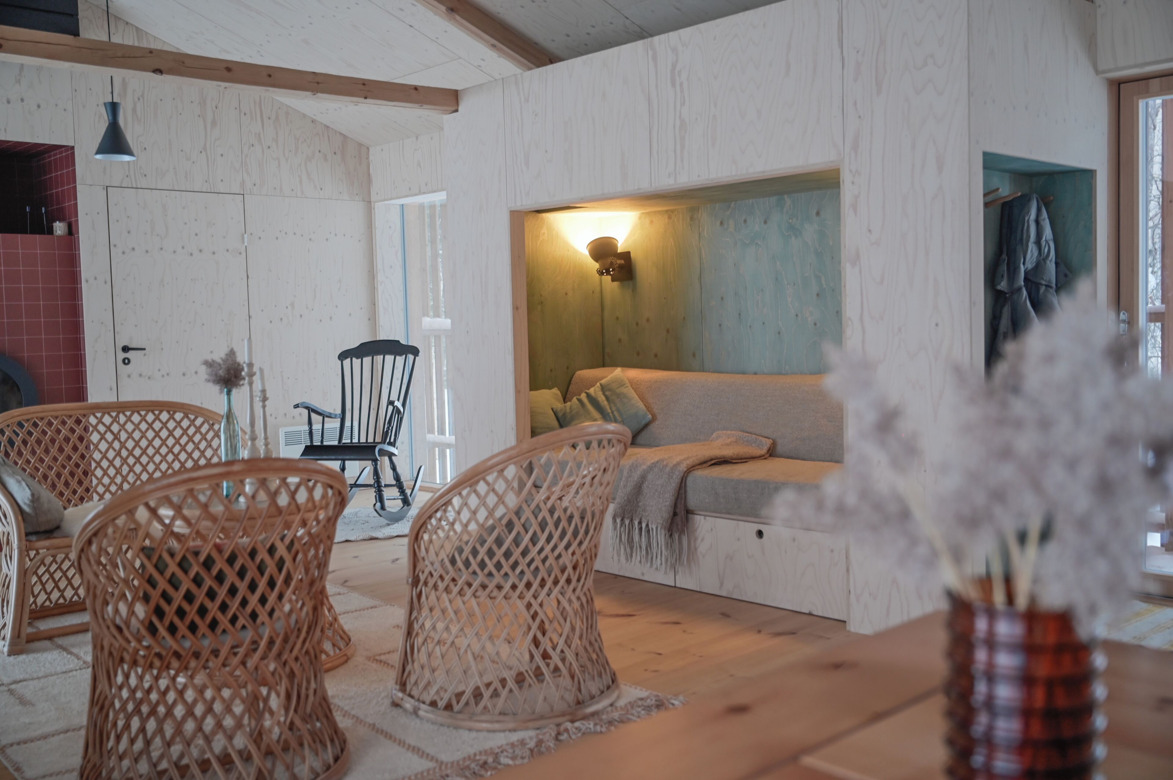 Une pièce chaleureuse avec un plancher en bois, un canapé agrémenté de coussins, des chaises en osier et une table sur laquelle est posé un vase rempli de fleurs séchées.