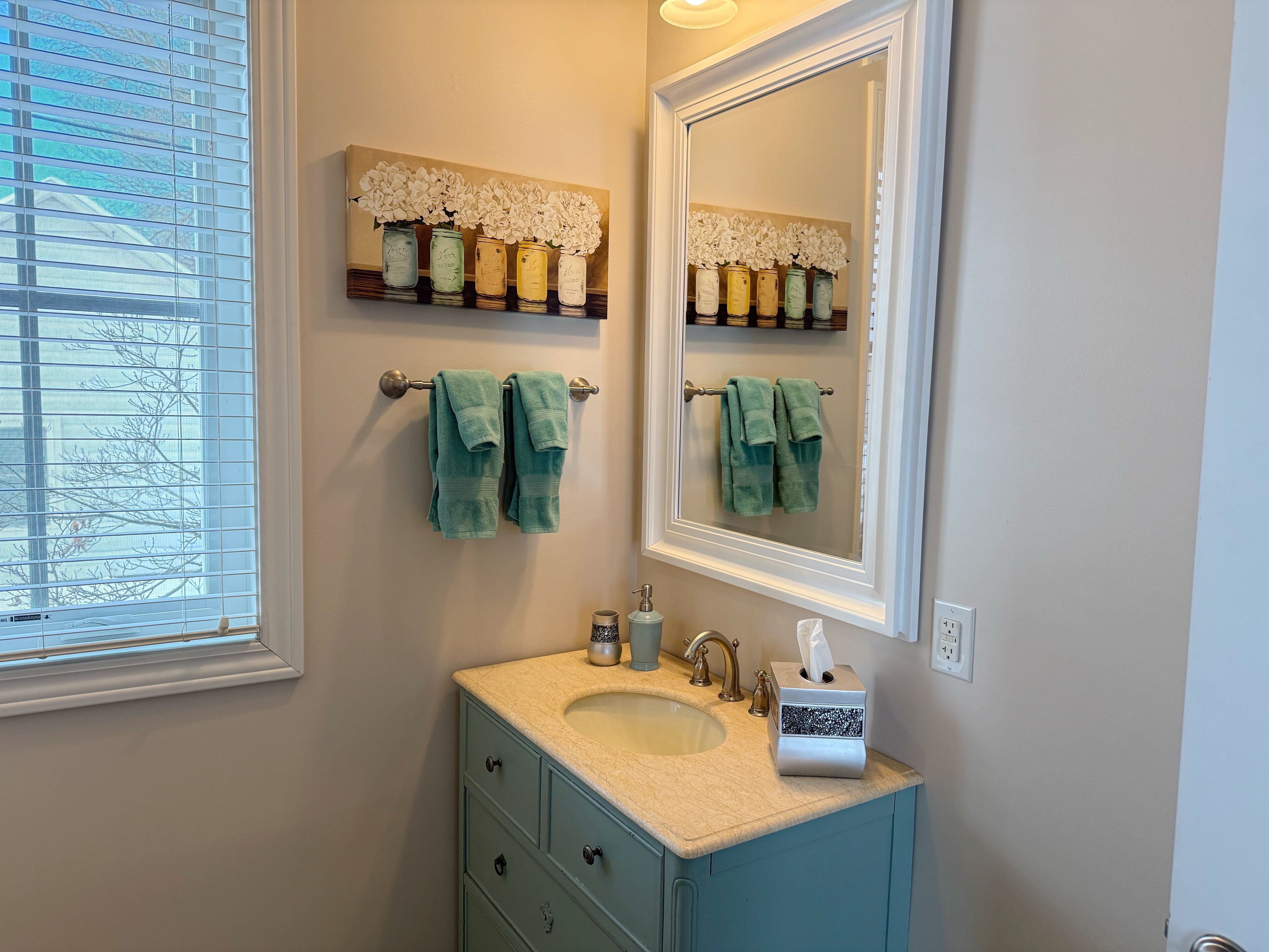 A bathroom with a sink, mirror, towel rack, and a window with blinds.