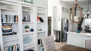 Una sala moderna con una estantería blanca, un sillón gris y una mesa de comedor de madera.