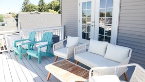 Una terraza con mobiliario exterior, incluyendo sillas y un sofá, una mesa de madera y una puerta blanca con paneles de vidrio.