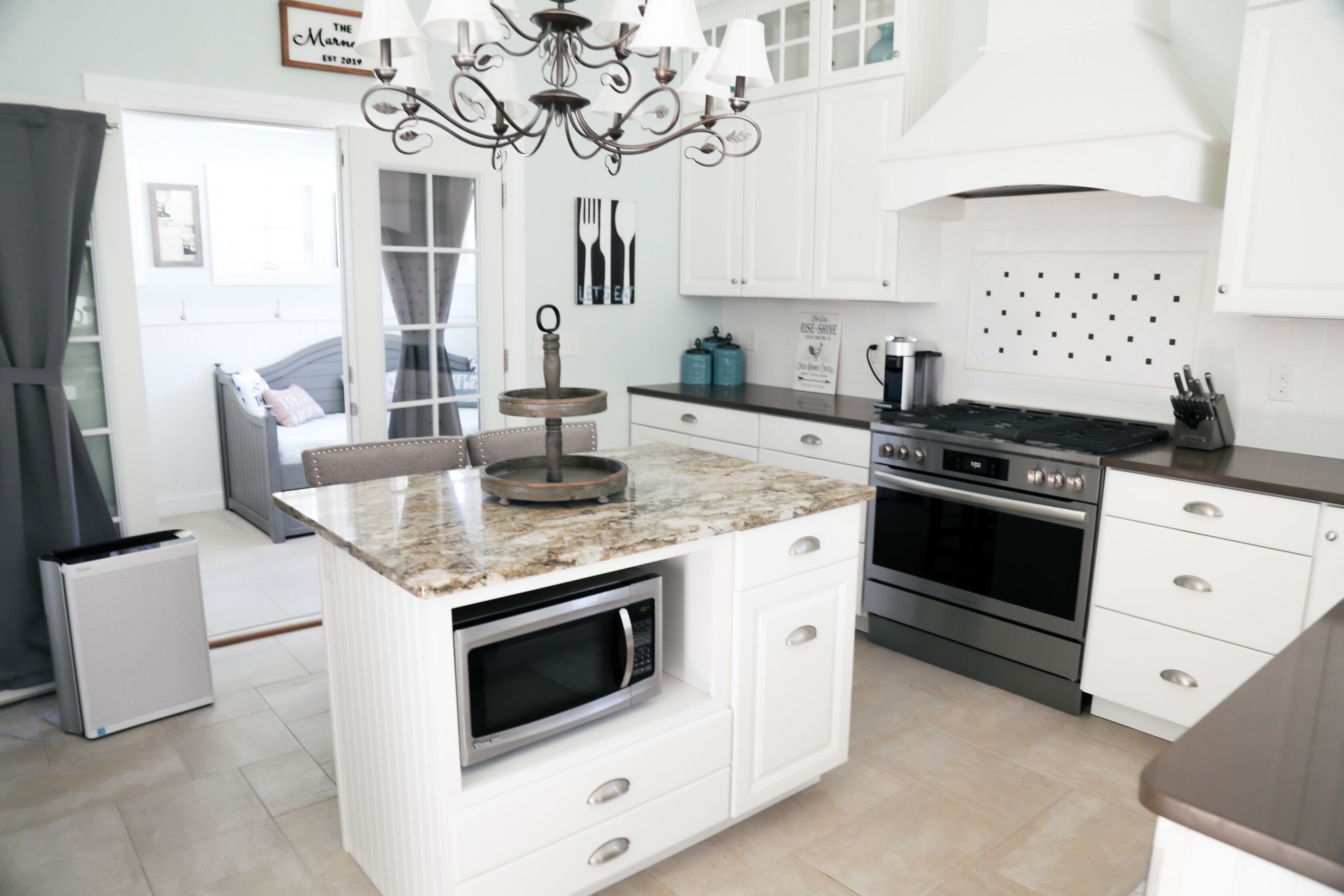 A modern kitchen with white cabinetry, a central island with a microwave, a gas stove, and a chandelier.