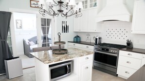 Una cocina moderna con armarios blancos, una isla central con microondas, estufa a gas y una araña.