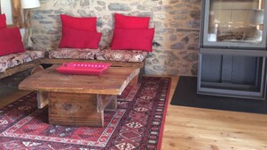 Ein gemütliches Wohnzimmer mit Steinwand, einer Couch mit roten Kissen, einem Holztisch und einem Kamin.