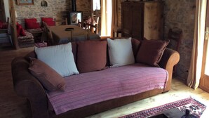 Ein gemütliches Wohnzimmer mit braunem Sofa, einer Steinwand, einem Holzschrank und einem Tisch mit Stühlen.