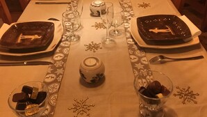 Ein Esstisch für vier Personen, gedeckt mit Tellern, Gläsern und Besteck. Auf der Tischdecke sind dekorative Schneeflockenmuster zu sehen.