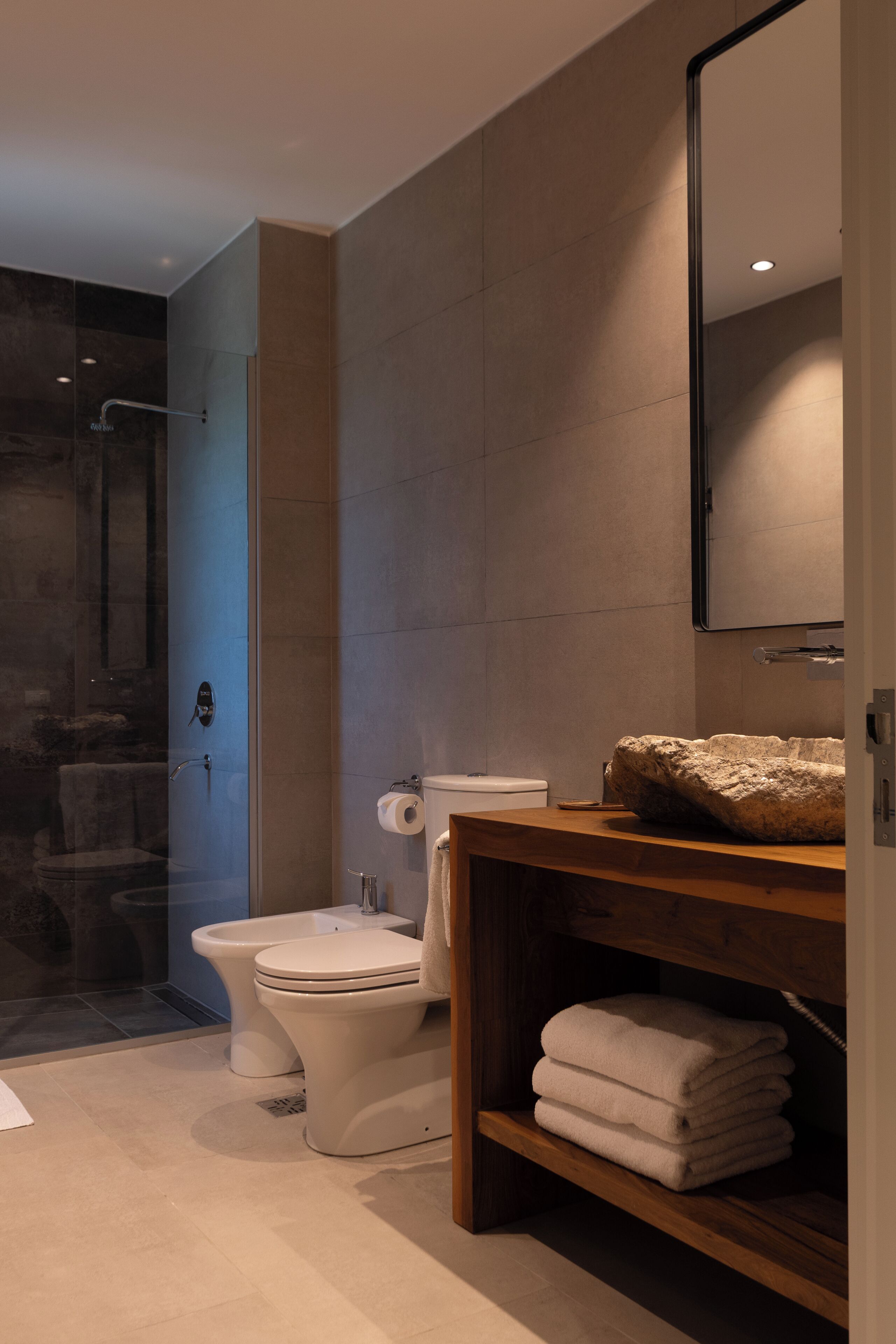 Un baño moderno con ducha de vidrio, inodoro y tocador de madera con toallas.