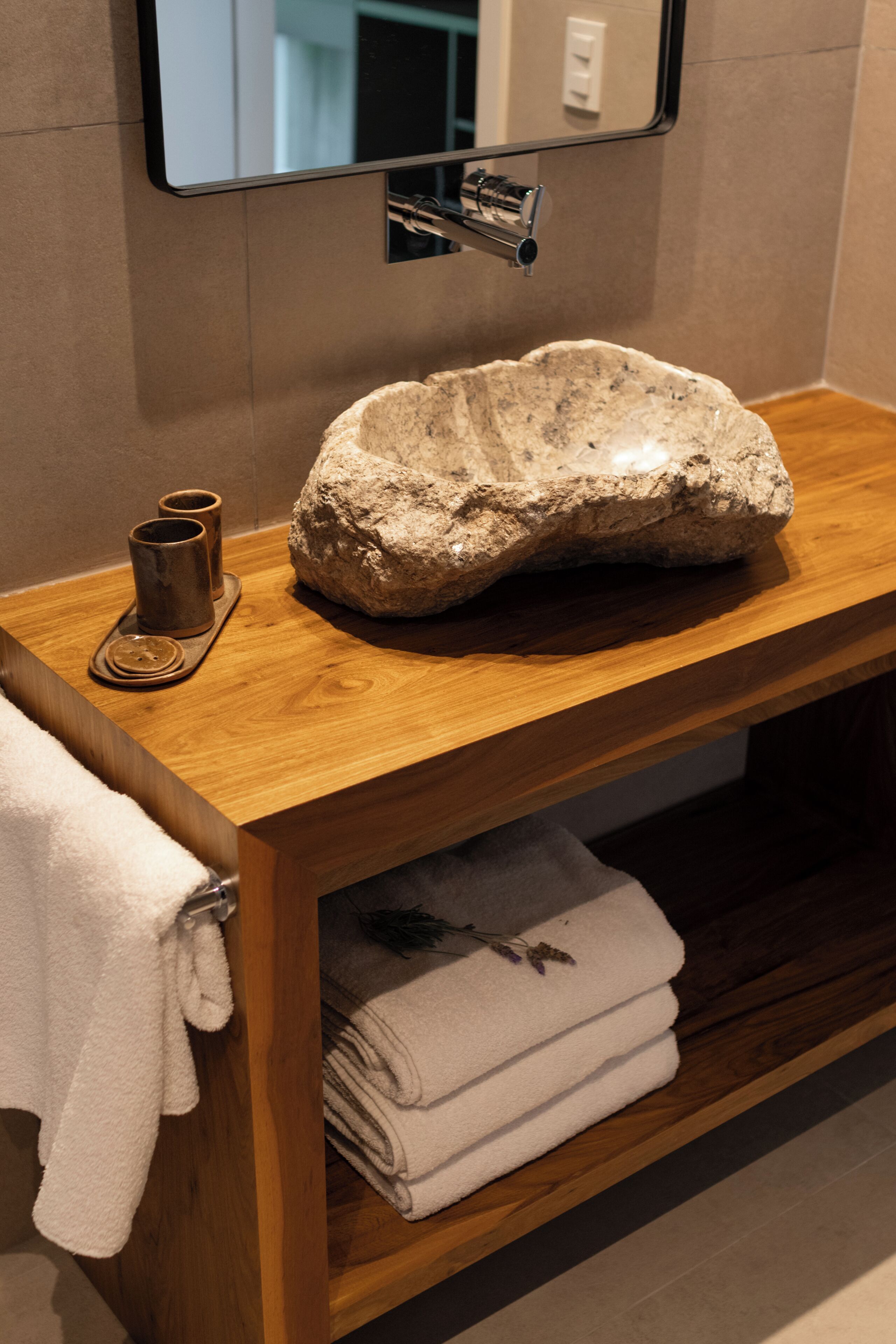 Un baño con tocador de madera, lavamanos de piedra, espejo y toallas.