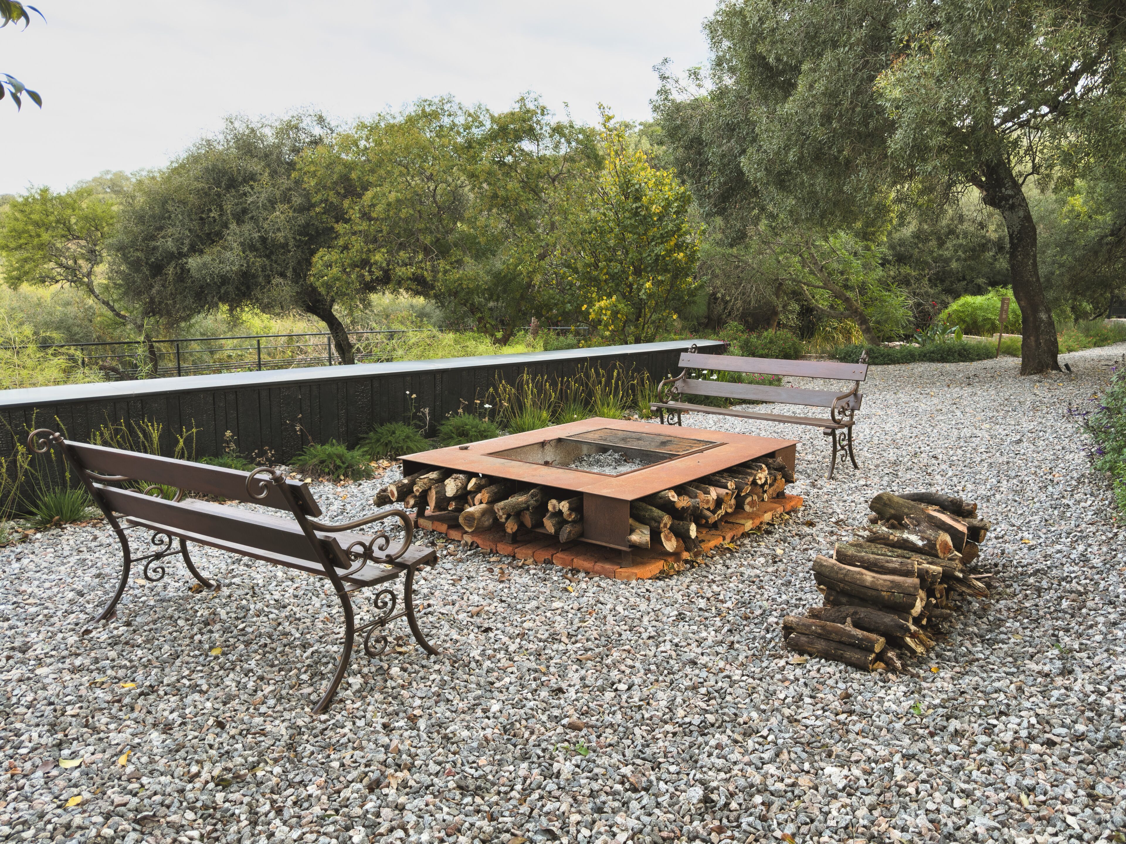 An outdoor seating area with benches and a fire pit surrounded by gravel.