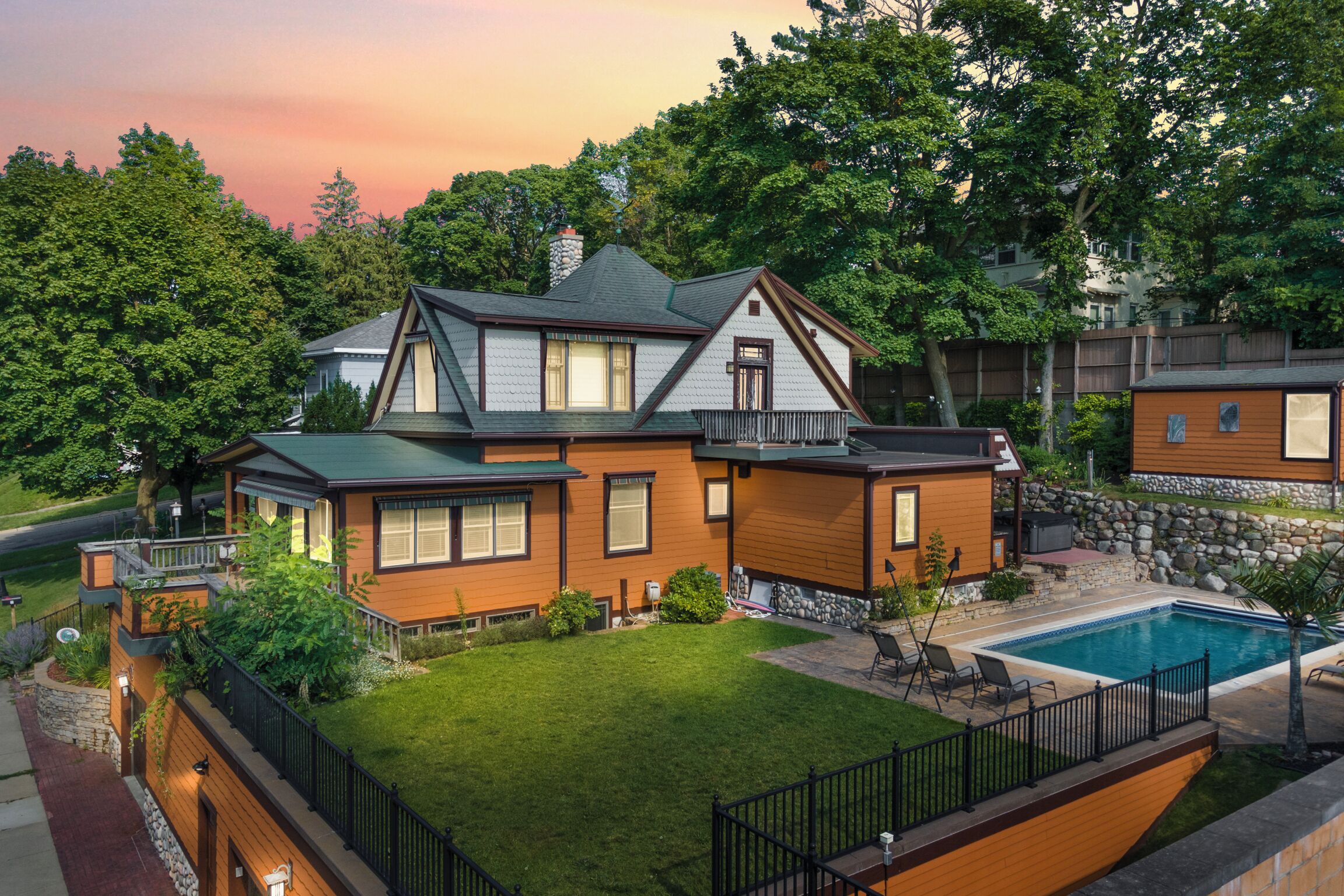 A two-story house with a large backyard, a swimming pool, and a stone wall.