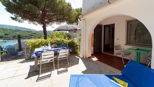 An outdoor patio with a table and chairs, a view of the lake, and a large tree. - Pal Friul - Villa Marinella (Mola)