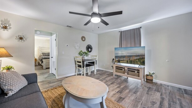 A modern living room with a ceiling fan, a dining table, and a large window with a view. - Charming 1-bedroom chalet in Melbourne awaits you. (Melbourne)