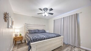 A bedroom with a wooden bed, a nightstand with a lamp, a ceiling fan, and a window with curtains. - Charming 1-bedroom chalet in Melbourne awaits you. (Melbourne)