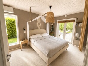 Ein Schlafzimmer mit Baldachinbett, Nachttisch, Pendelleuchte und Blick ins Freie.