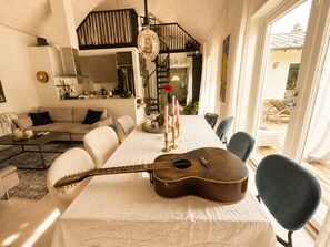 Ein Essbereich mit einem für sechs Personen gedeckten Tisch, einer Gitarre auf dem Tisch und einer Treppe, die zu einer oberen Ebene führt.