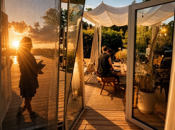Ein moderner Essbereich im Freien mit Glasveranda, Holzterrasse und Sonnenuntergangsblick.