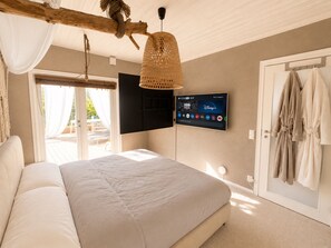 Ein Schlafzimmer mit einem Bett, einem an der Wand befestigten Fernseher und einer Tür, an der Bademäntel hängen.