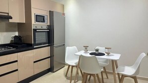 A modern kitchen with beige cabinetry, a black countertop, and a dining area with white chairs and a small table. - Z House Gueliz  Marrakech (Marrakech)