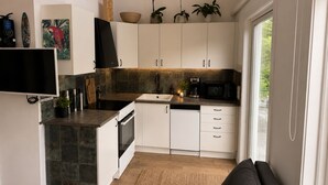 Una cocina moderna con armarios blancos, una estufa negra, un fregadero y un microondas. Hay un televisor de pantalla plana montado en la pared, y se observan diversos utensilios de cocina.