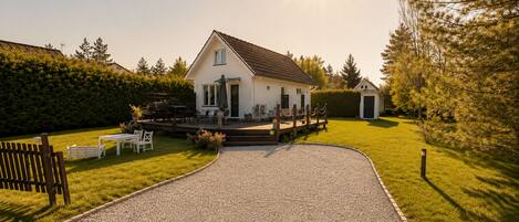 A house with a gravel driveway, a deck with outdoor furniture, and a small shed in the background.