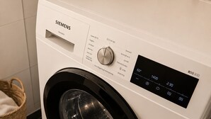 Una lavadora Siemens en un baño con suelo de baldosas, una cesta y un tendedero.