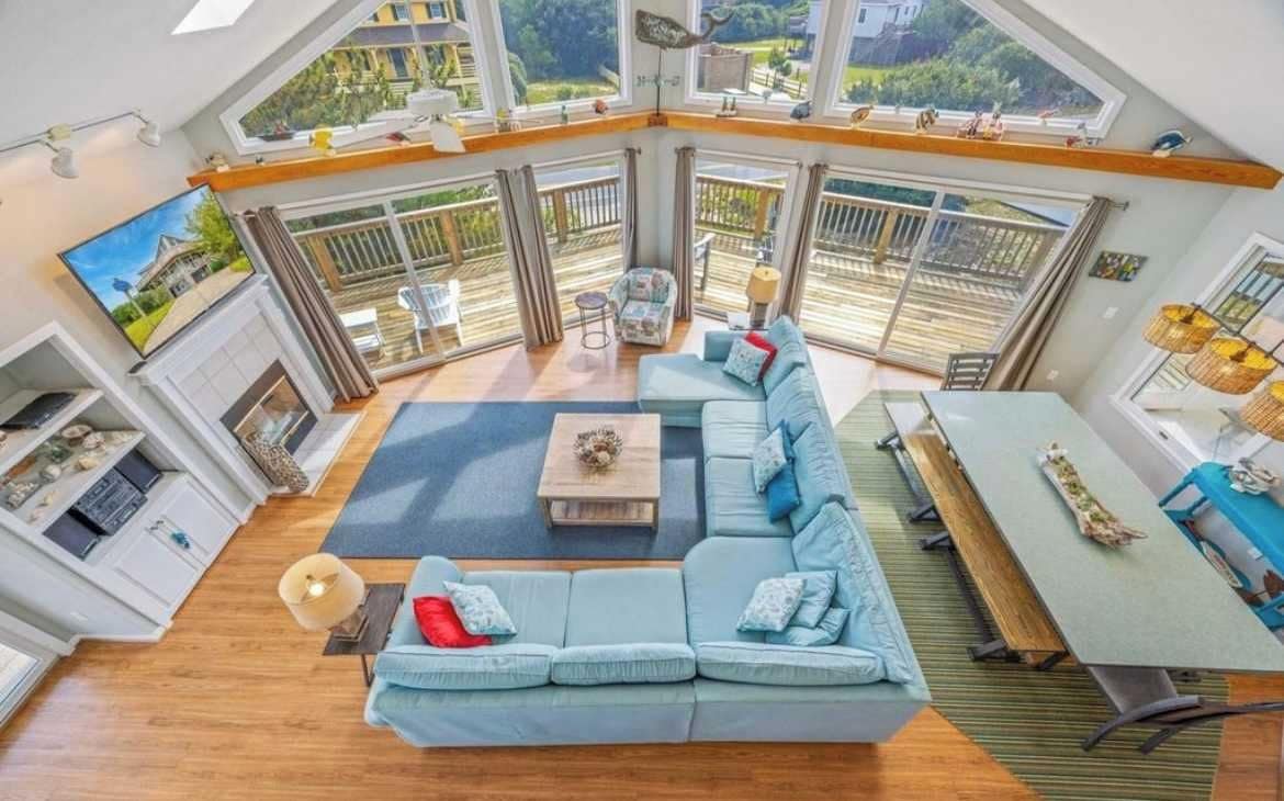 A spacious living area with a large sofa, a dining table, and a view of the outdoors through large windows.
