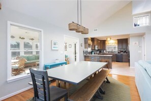 A modern kitchen with a central island, a dining area with a large table, and a cozy seating area with a sofa. - Pool, Hot Tub, EV Charger & 2-Min Walk to Beach! (Corolla)