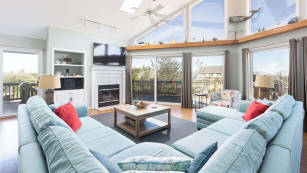 A spacious living room with a fireplace, large windows, and a balcony. - New Listing! Pool, Hot Tub & 2-Min Walk to Beach! (Corolla)