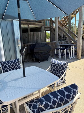 An outdoor patio area with a table and chairs, a covered grill, and a wooden staircase. - Pool, Hot Tub, EV Charger & 2-Min Walk to Beach! (Corolla)